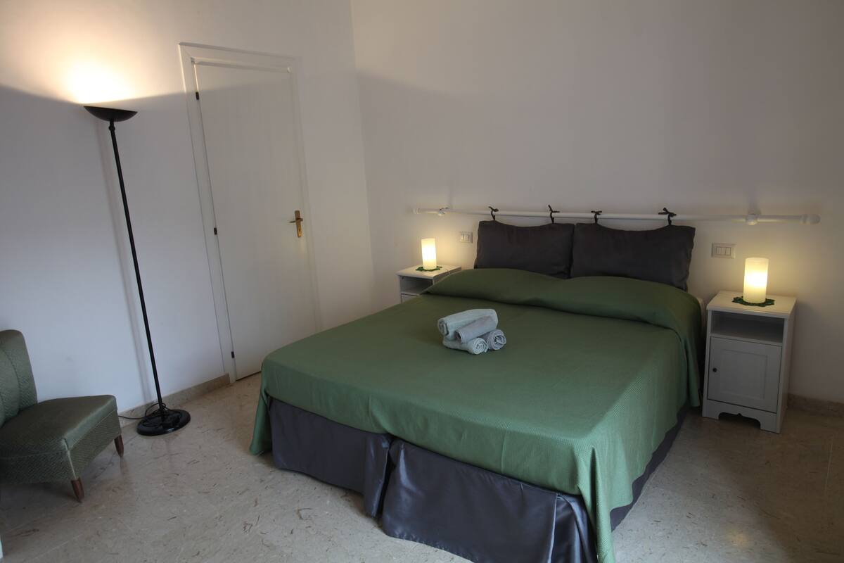 Une chambre bien rangée, avec un lit, deux tables de chevet, une lampe sur pied et une chaise.