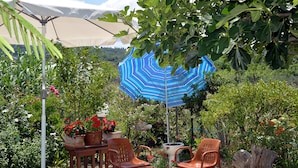 An outdoor seating area with a table, chairs, and a blue-striped umbrella providing shade. - Feeloxenia Corfu Apartments (Corfu)