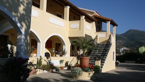 A two-story building with a balcony, a staircase, and a garden with various plants. - Feeloxenia Corfu Apartments (Corfu)