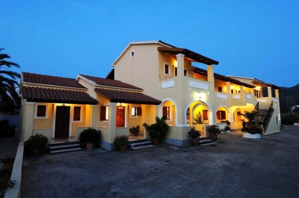 A two-story building with a tiled roof, multiple windows, and a central entrance with steps. - Feeloxenia Corfu Apartments (Corfu)