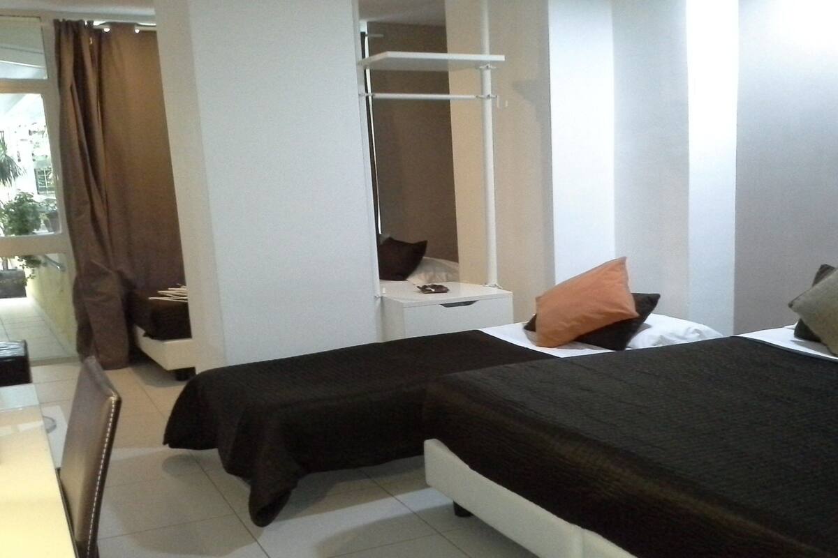 Una camera d'albergo con due letti, un comodino, una sedia, uno specchio e un quadro appeso al muro.