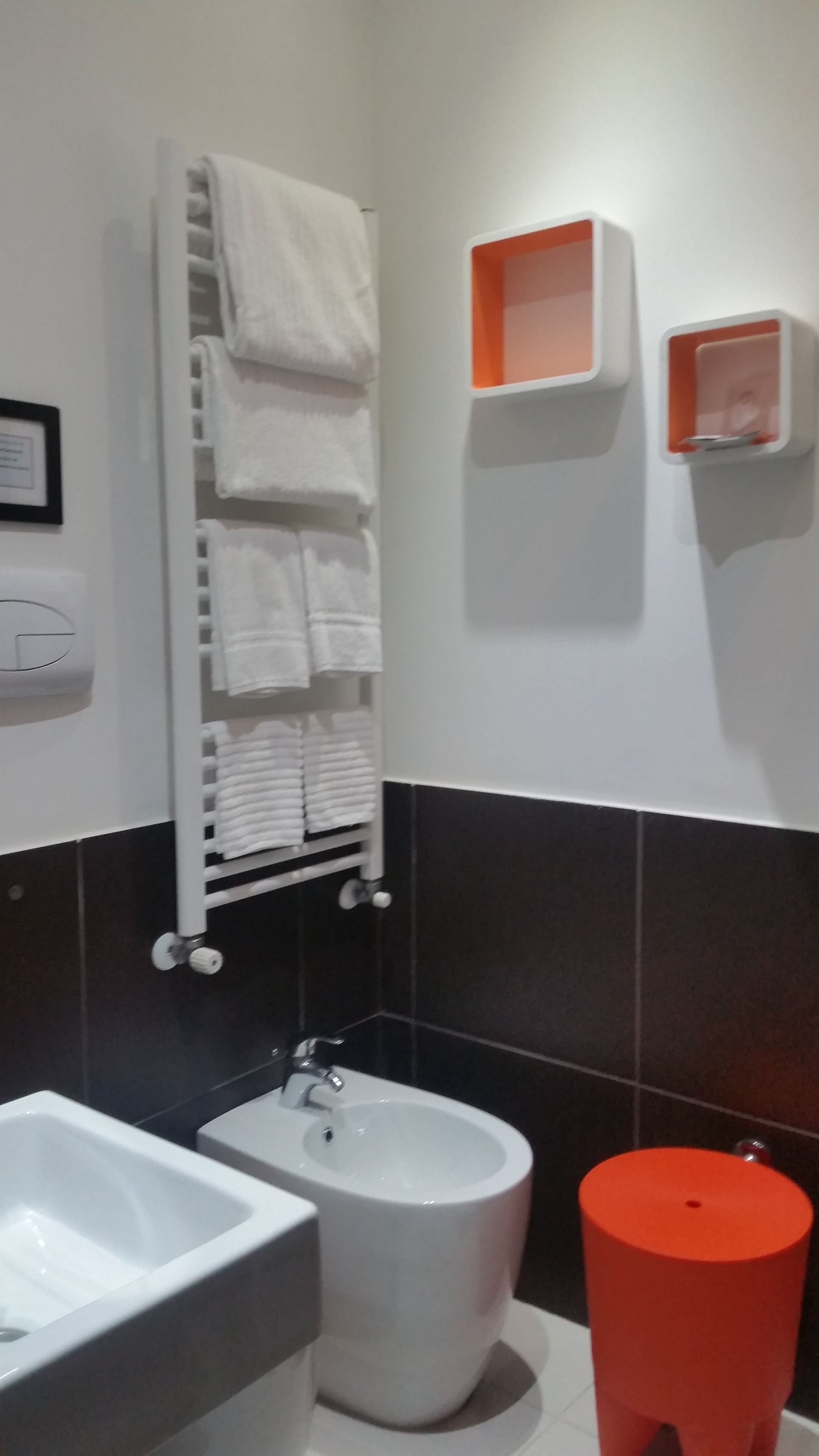 Casa de banho com lavatório branco, bidé, um porta-toalhas com vários toalhas e um lixo vermelho.