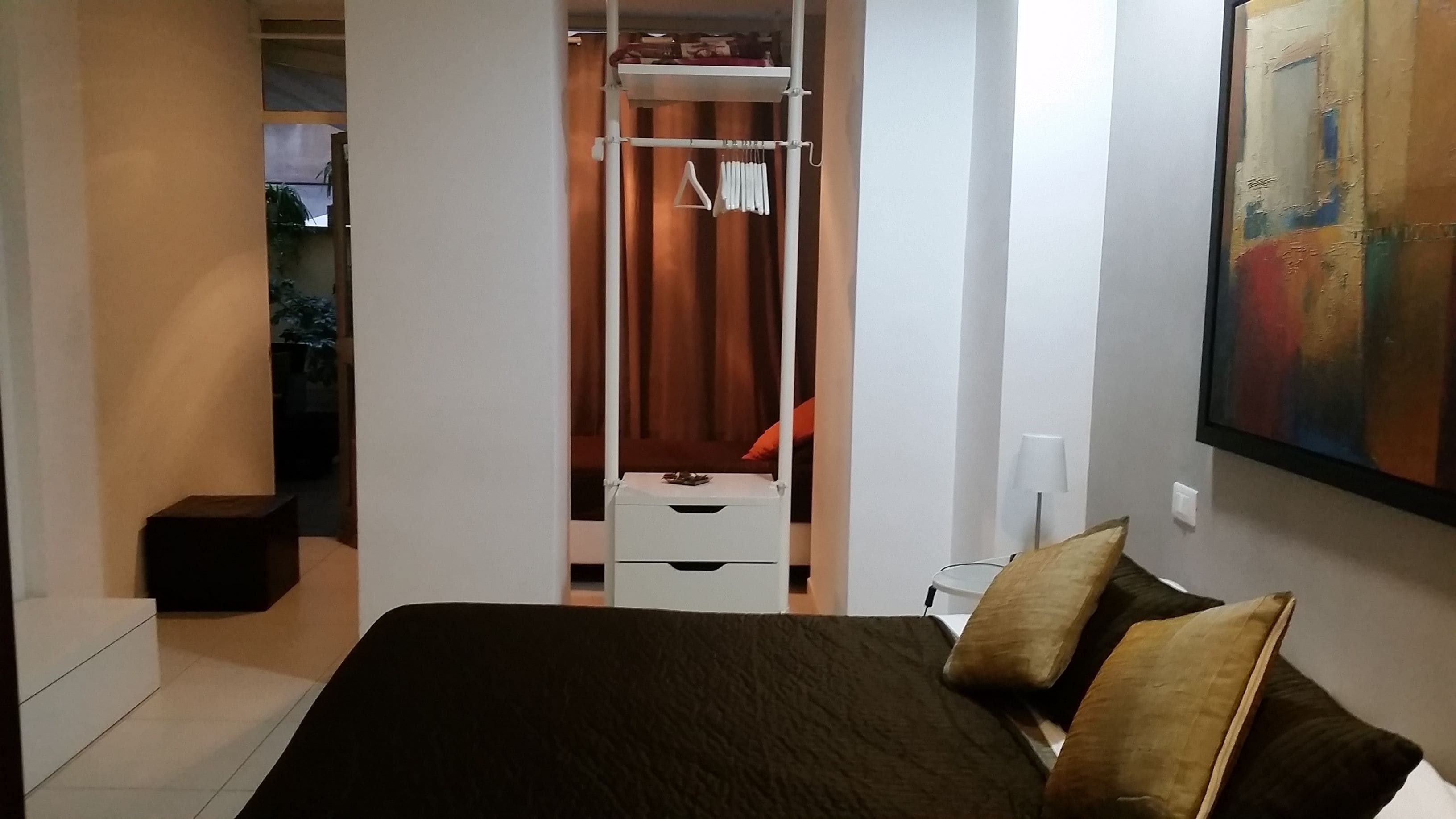 A bedroom with a bed, a wardrobe, a nightstand, and a painting on the wall.