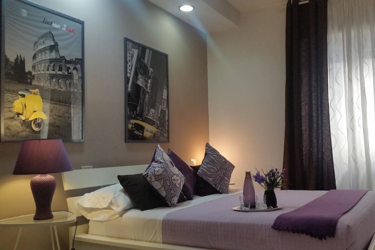 Una camera d'albergo ordinata con un letto, un comodino con una lampada e due quadri appesi al muro.