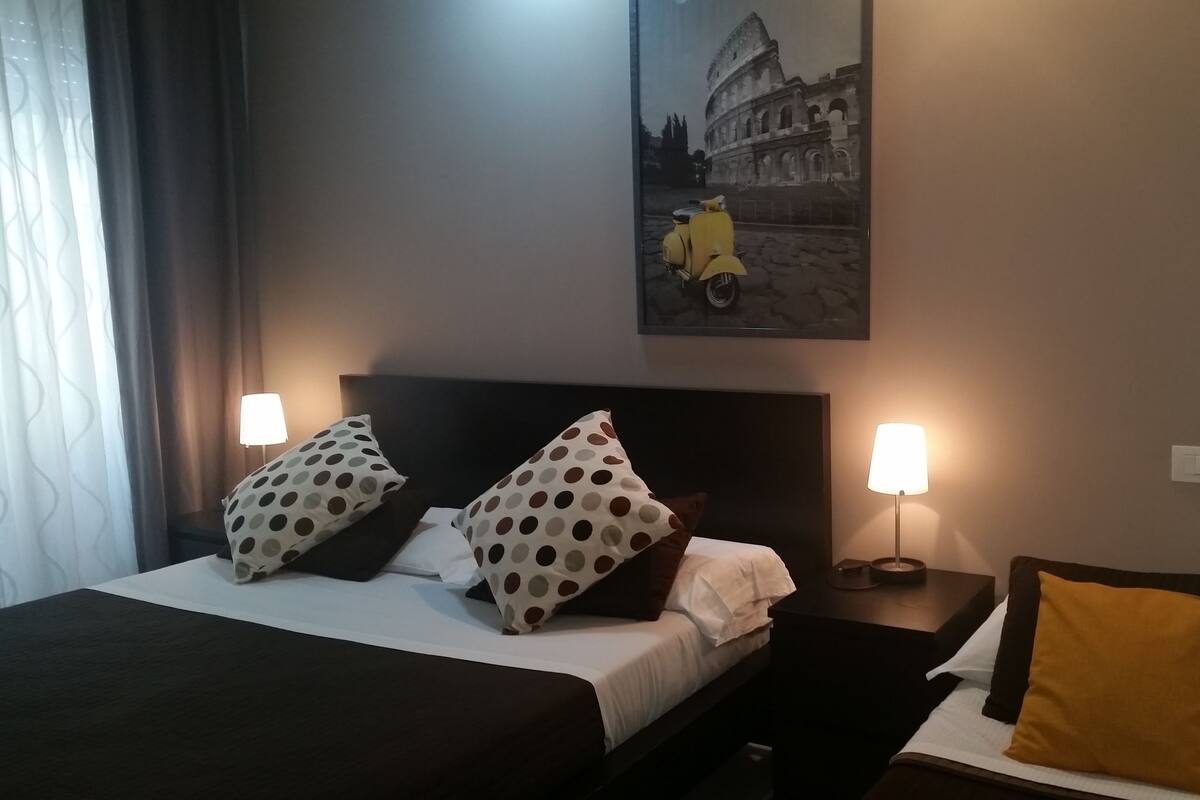 Una camera d'albergo con un letto, due comodini, una lampada e un quadro che raffigura il Colosseo.