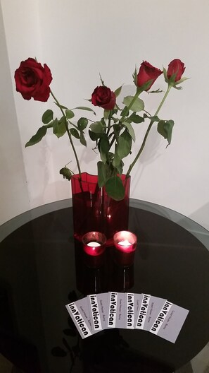 A table with a red vase containing roses and two lit candles. - InnVatican (Rome)