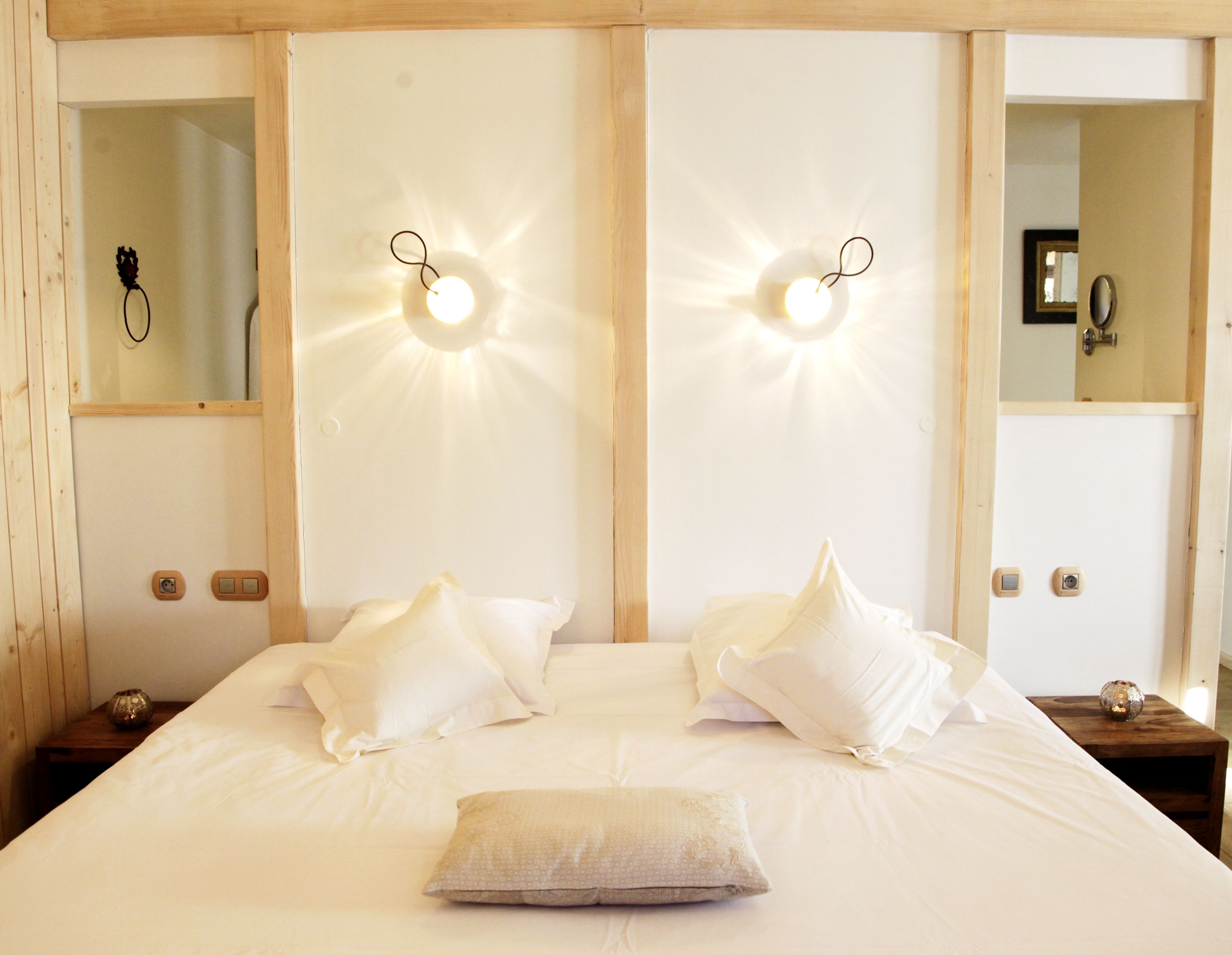 A neatly made bed with white linens and pillows, a bedside table with a decorative item, and wall-mounted lights.