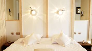 A neatly made bed with white linens and pillows, a bedside table with a decorative item, and wall-mounted lights.
