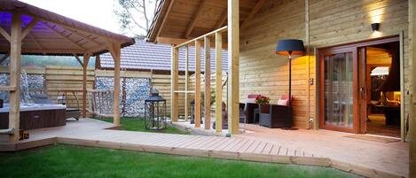 A wooden cabin with a covered patio, outdoor seating, and a hot tub.
