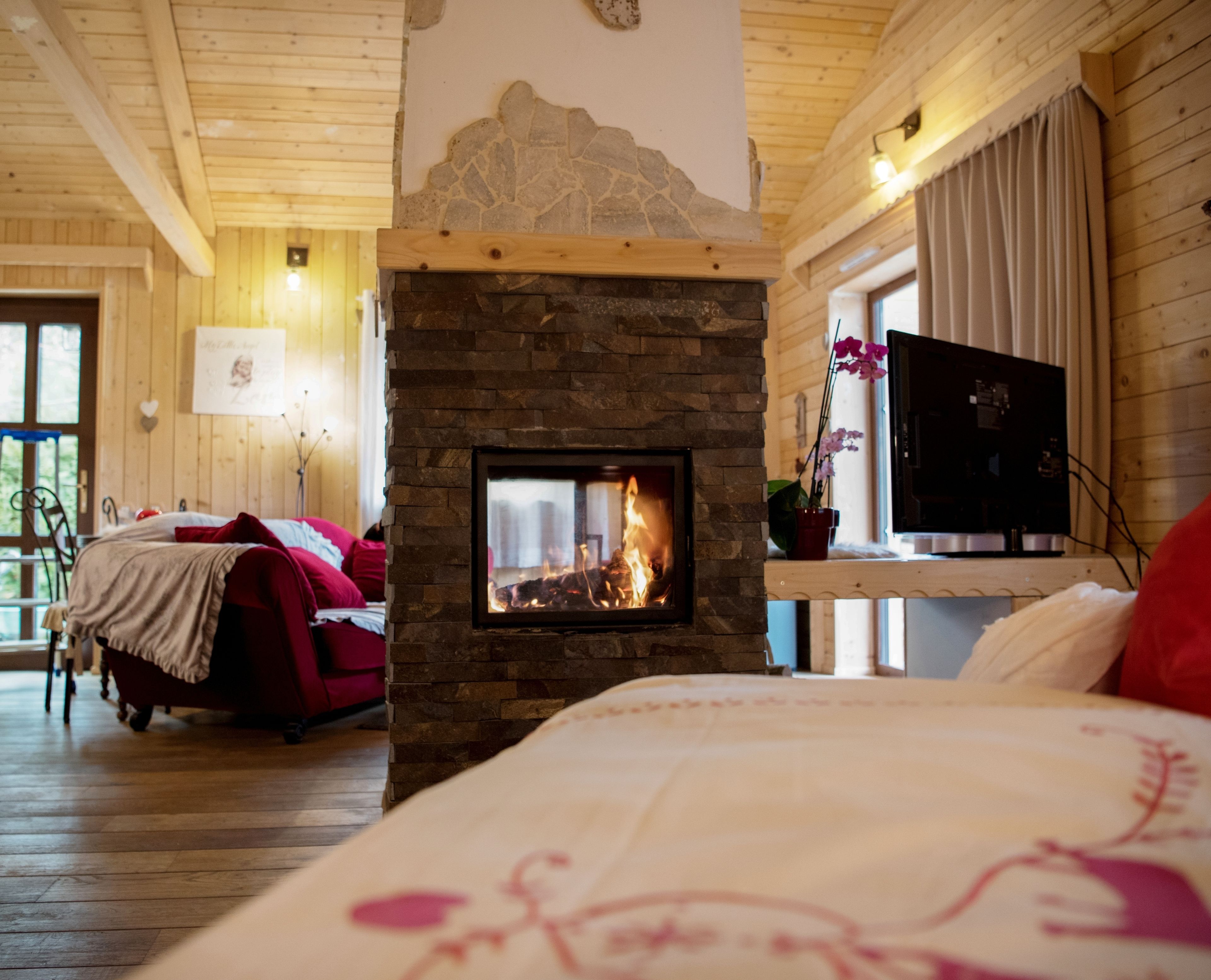 A cozy room with a stone fireplace, wooden ceiling, and a bed with floral bedding.