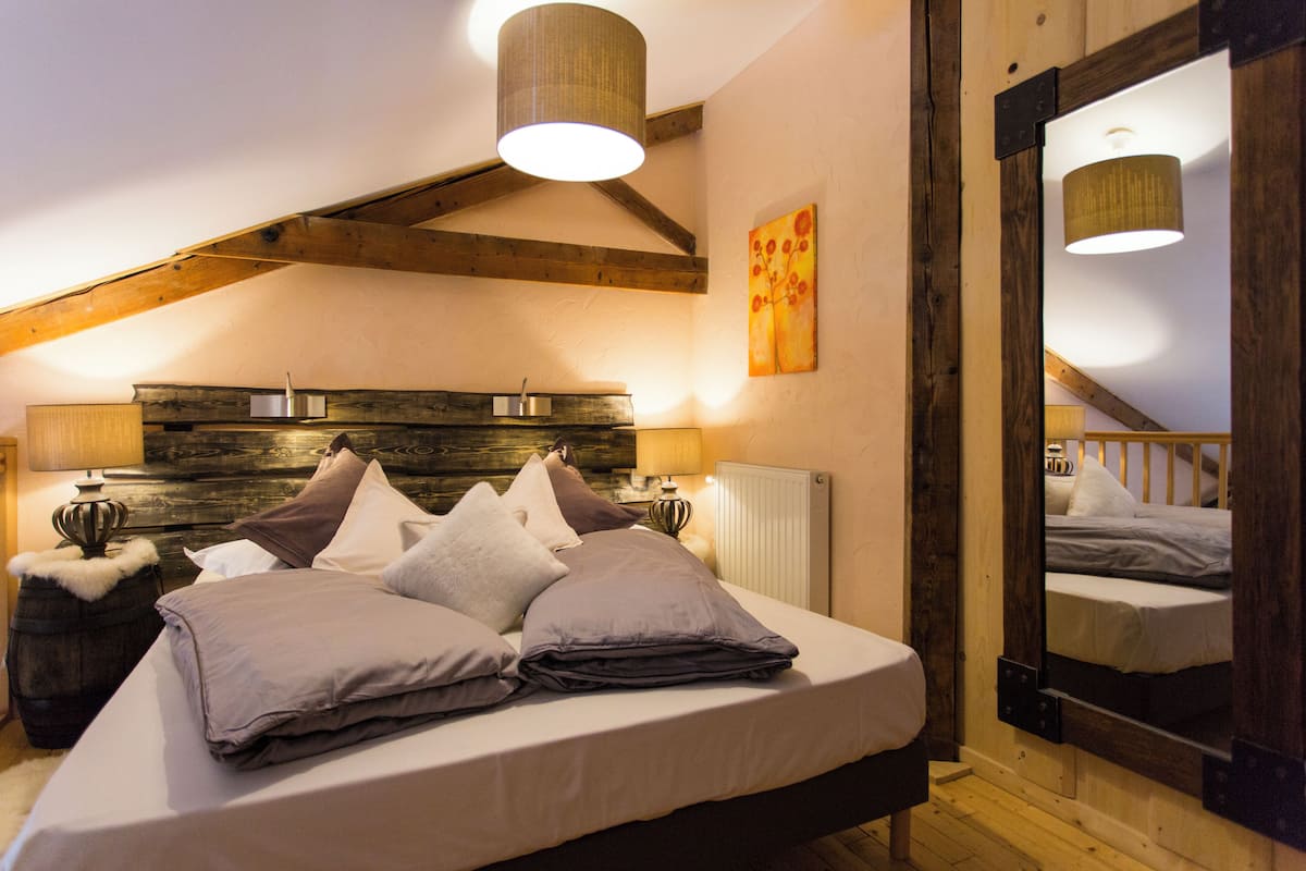 A bedroom with a wooden headboard, a large bed with multiple pillows, bedside lamps, and a mirror.