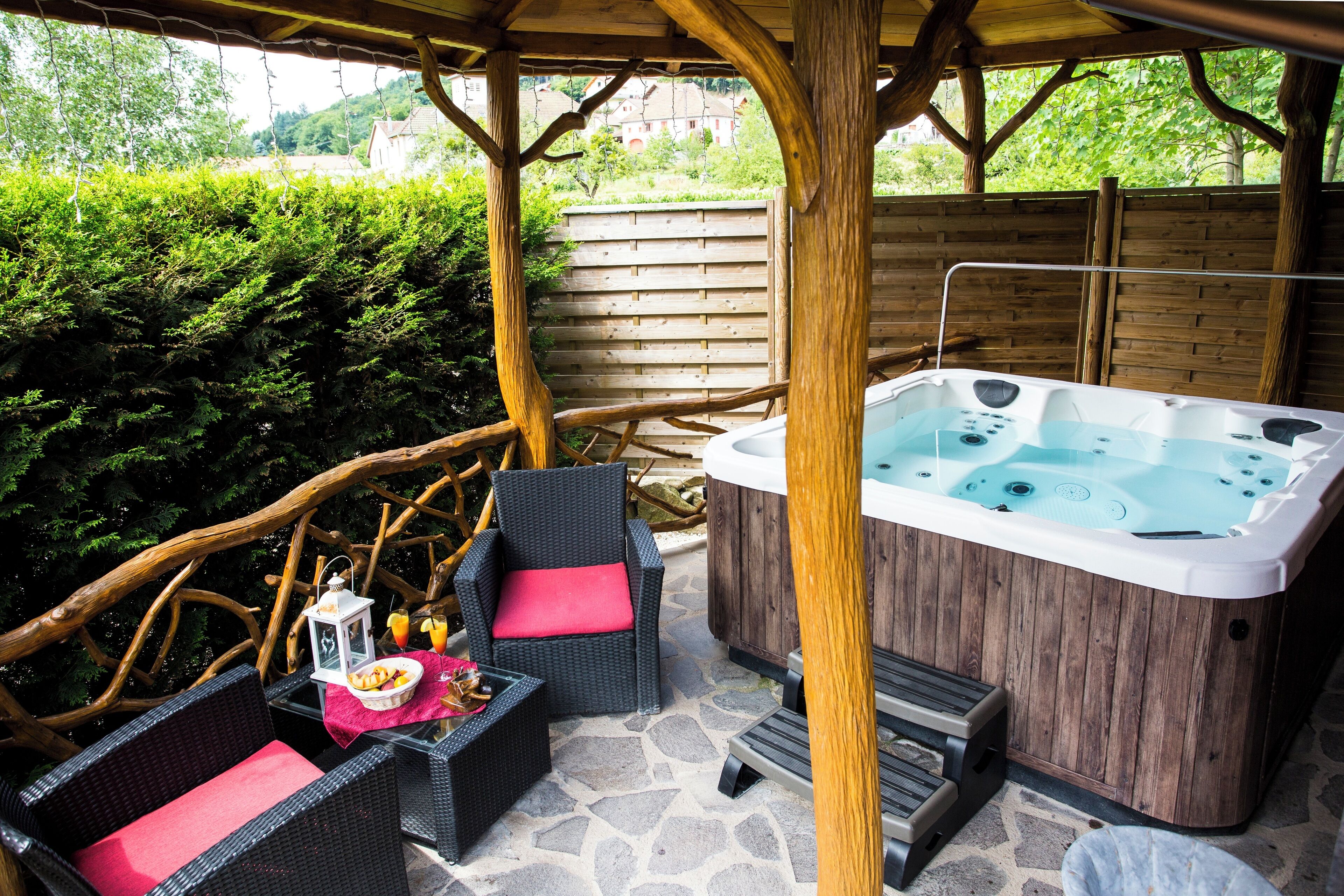 Un espace extérieur avec un jacuzzi, des fauteuils en osier, une terrasse en bois et un sol en pierre.