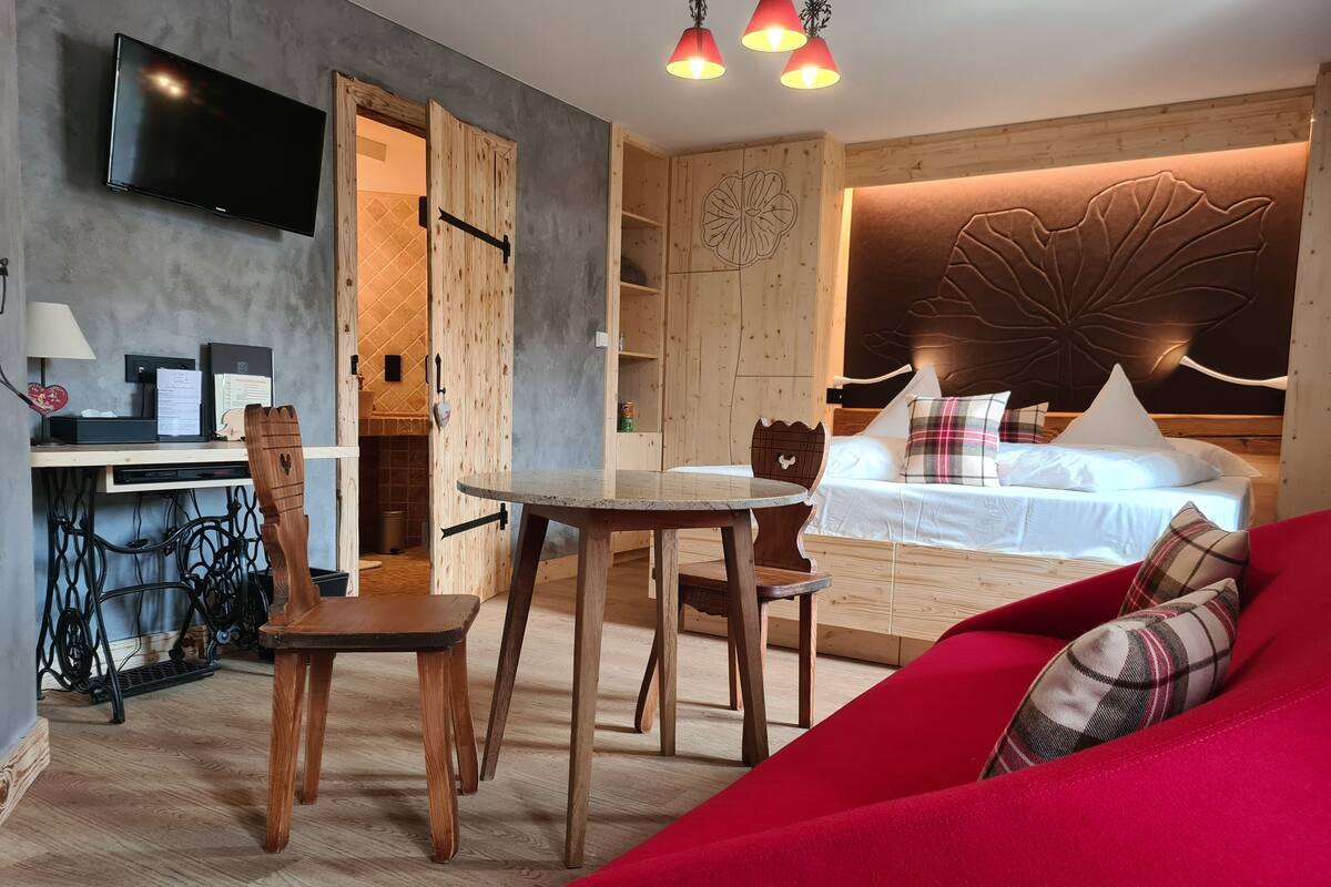 A modern room with a bed, a red sofa, a dining table with chairs, a TV mounted on the wall, and a wooden cabinet.