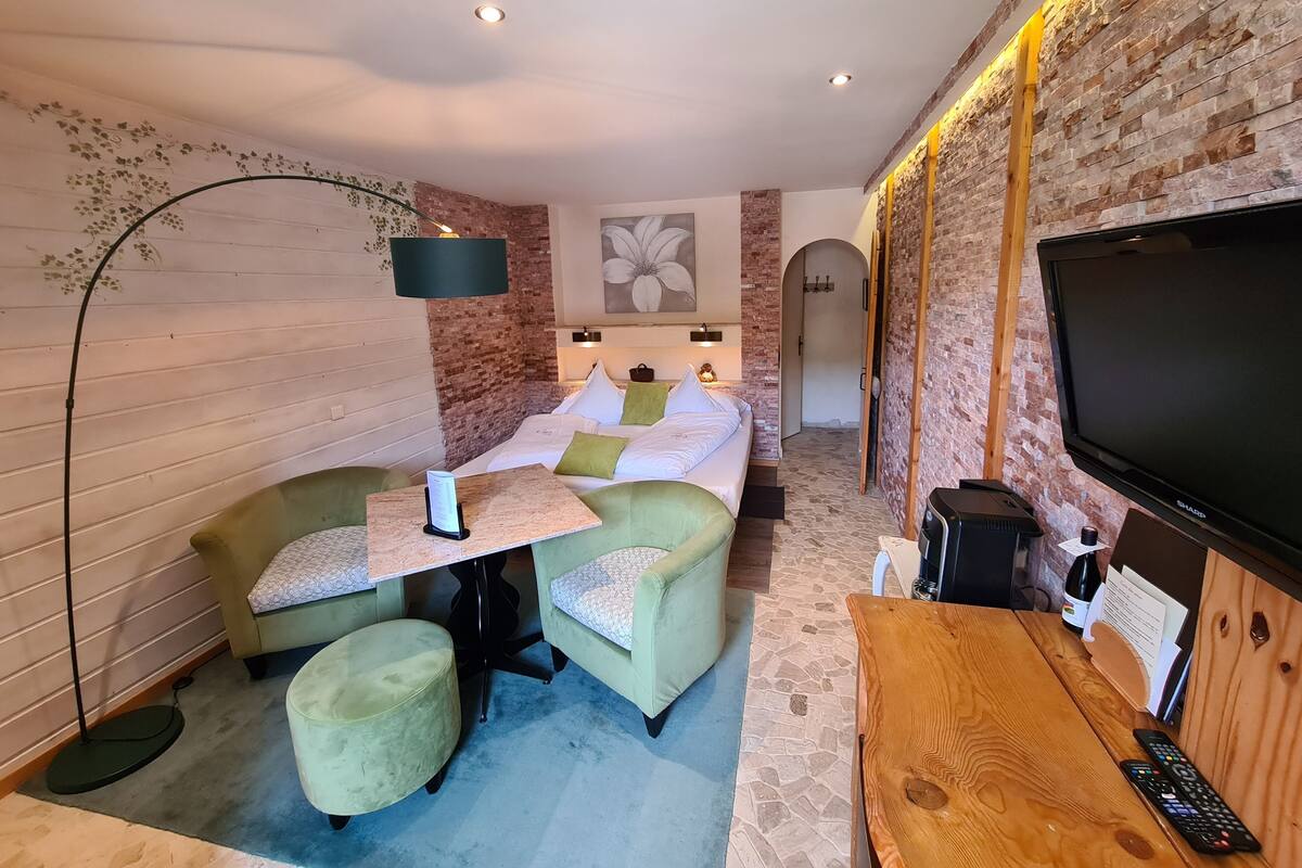 A cozy room with a bed, a small table, a TV, and a brick wall.