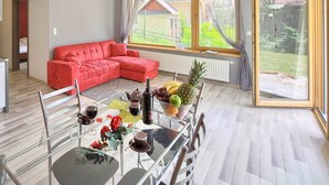 Ein modernes Wohnzimmer mit einem roten Sofa, einem Esstisch mit Stühlen und einem großen Fenster mit Blick auf einen Garten.