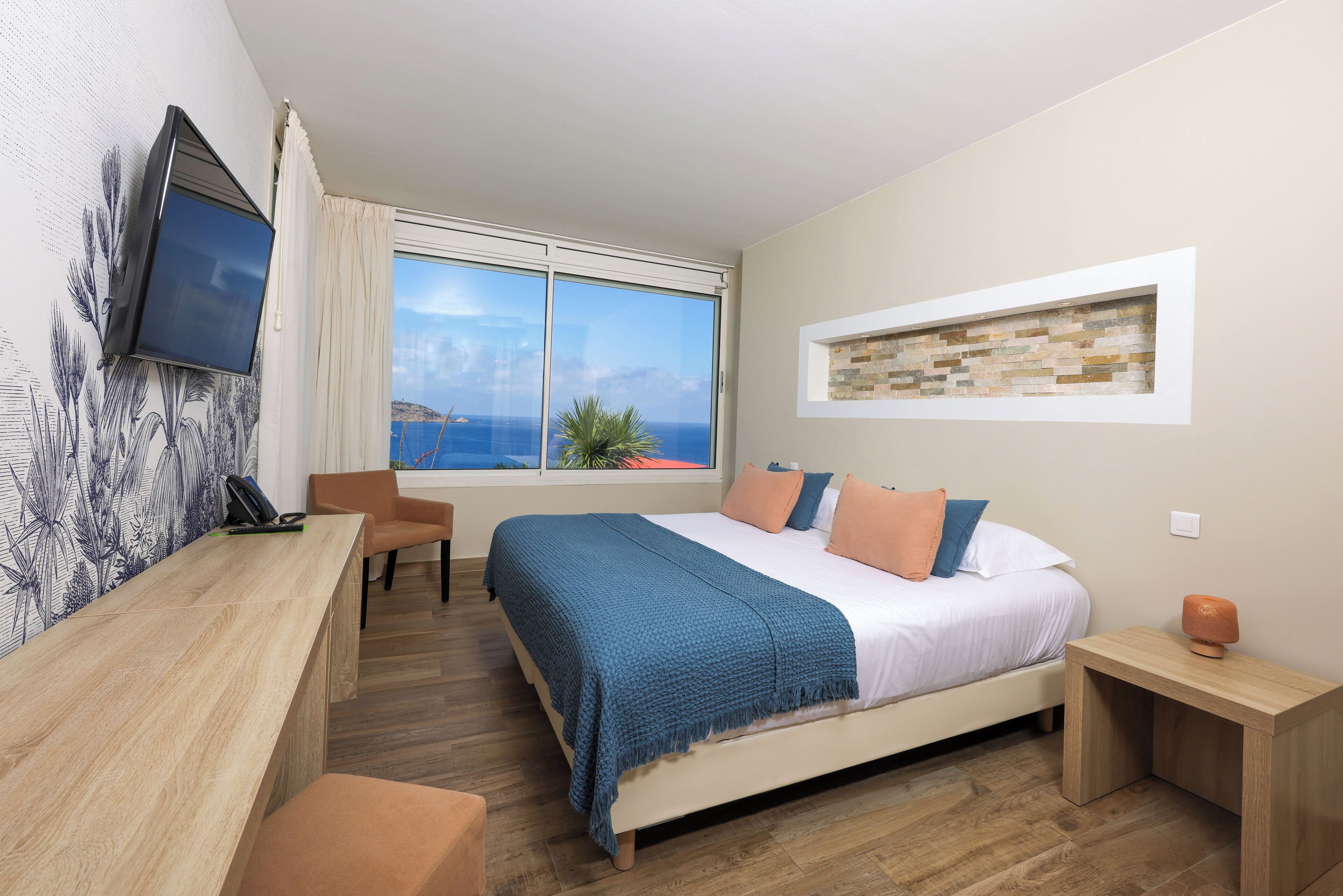 Un dormitorio con cama, escritorio, silla, televisor y ventana con vista al mar.