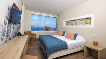 Un dormitorio con cama, escritorio, silla, televisor y ventana con vista al mar.