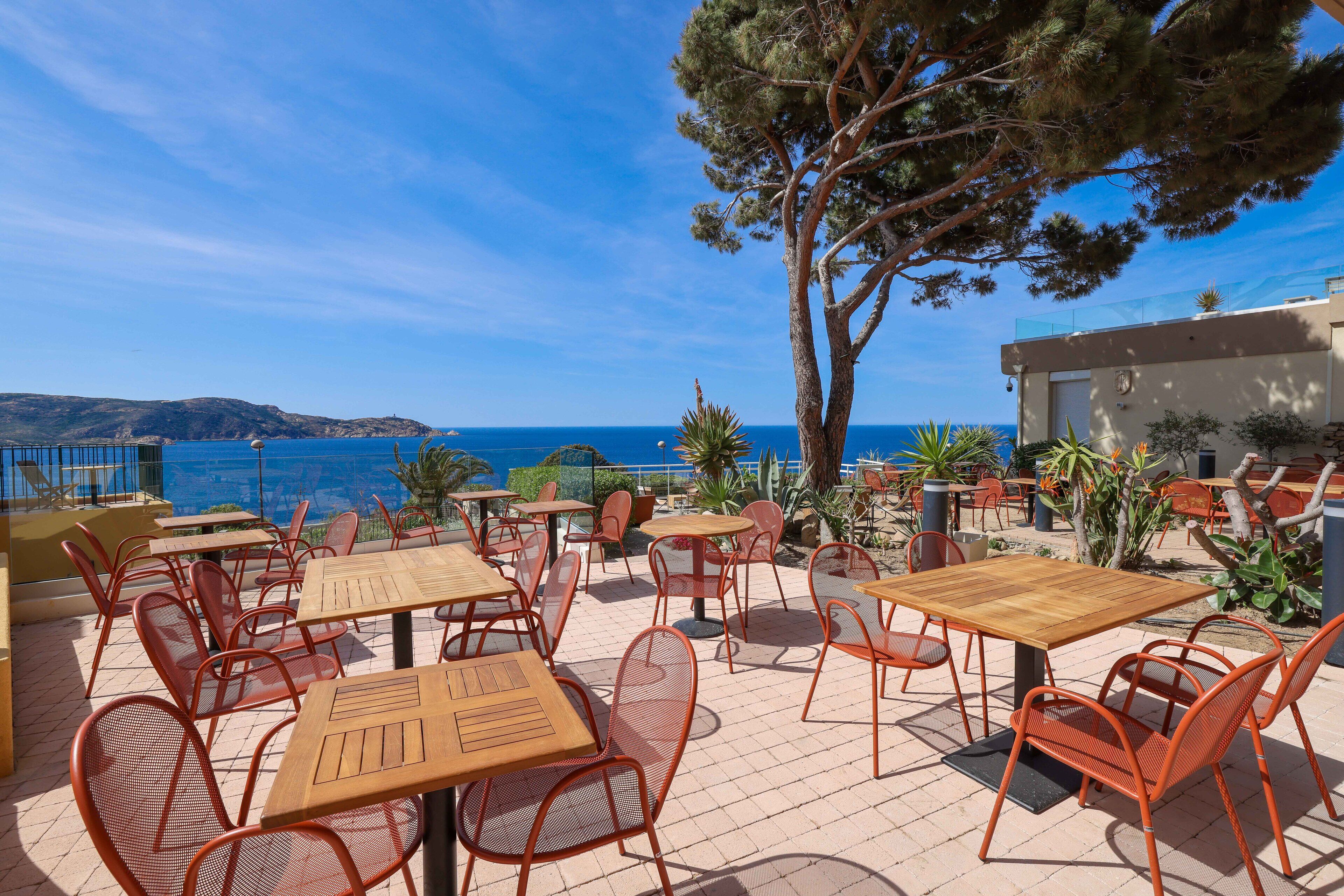 An outdoor patio with tables and chairs, overlooking a body of water and hills.