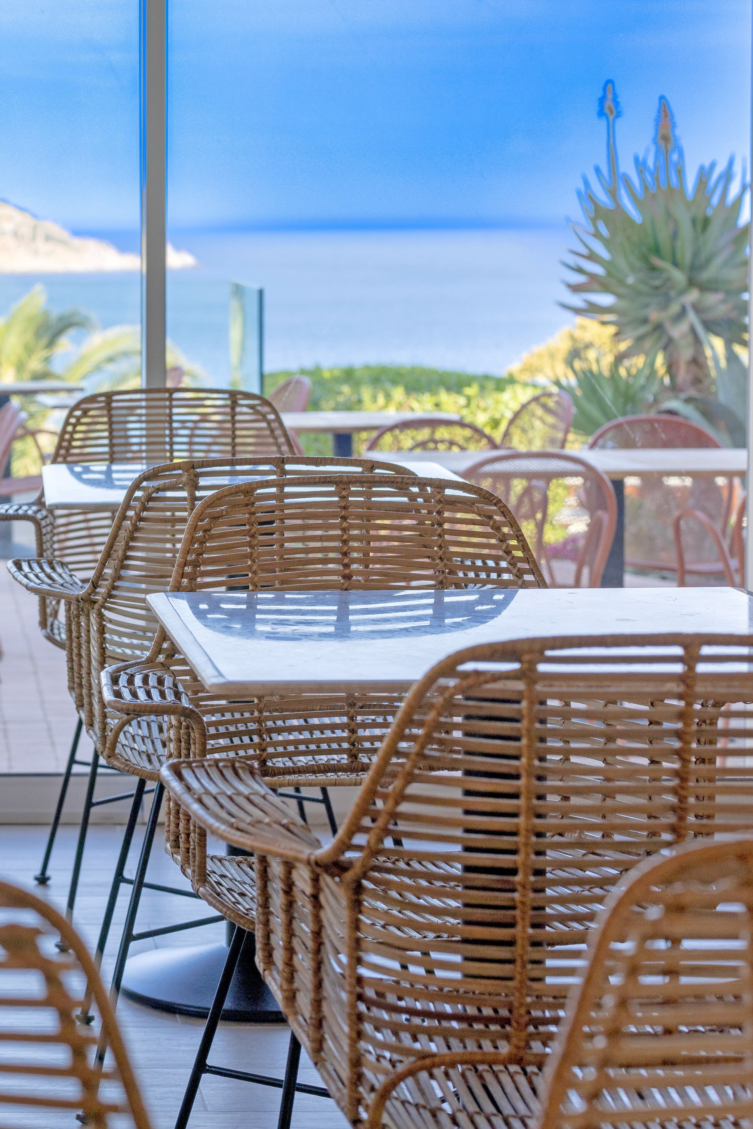 Wicker chairs and tables arranged on a terrace with a view of the ocean.