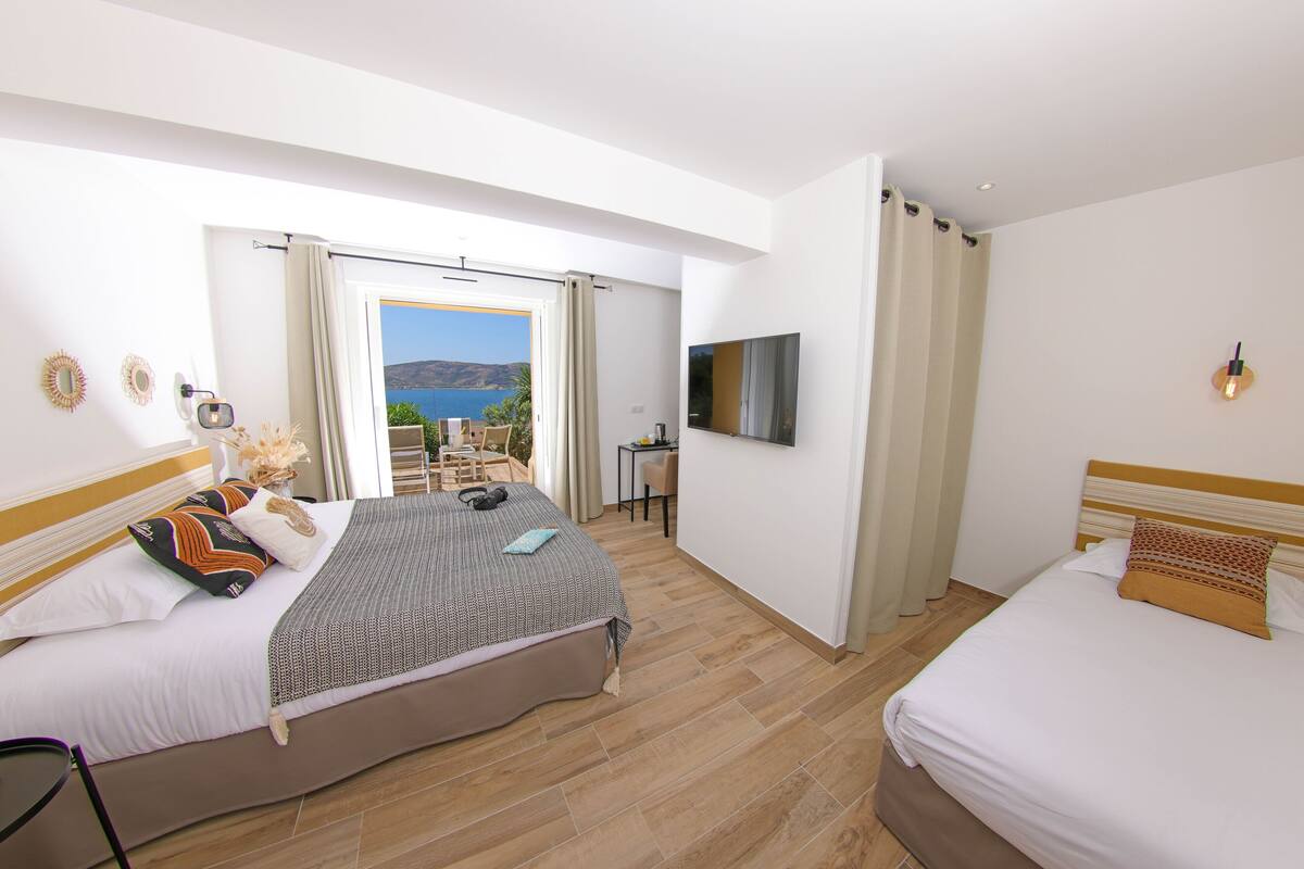Quarto de hotel com cama, uma cama adicional, televisão, escrivaninha e vista para o mar.