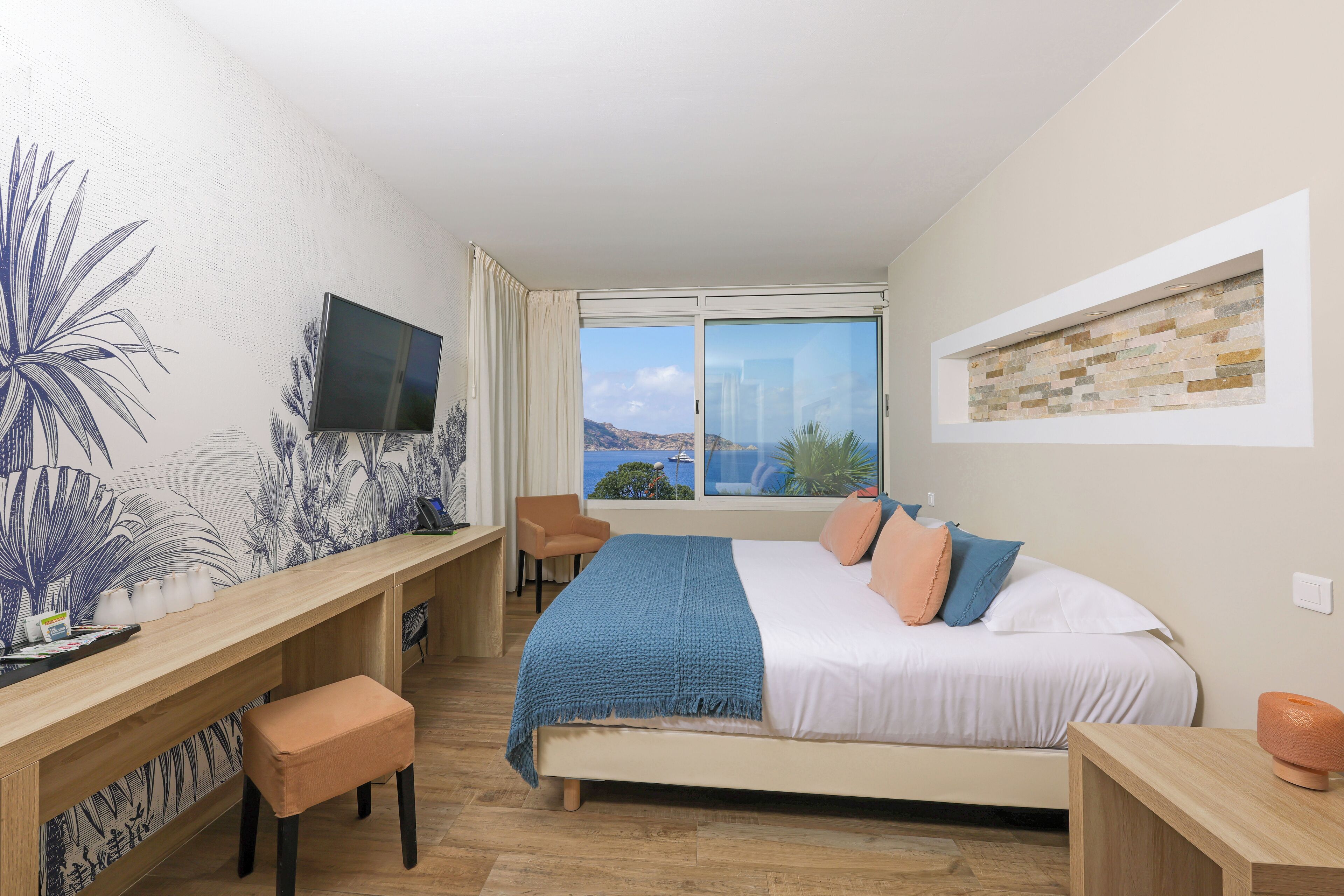 Un dormitorio con cama, escritorio, silla, televisor y ventana con vistas a las montañas.