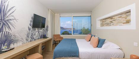 Un dormitorio con cama, escritorio, silla, televisor y ventana con vistas a las montañas.