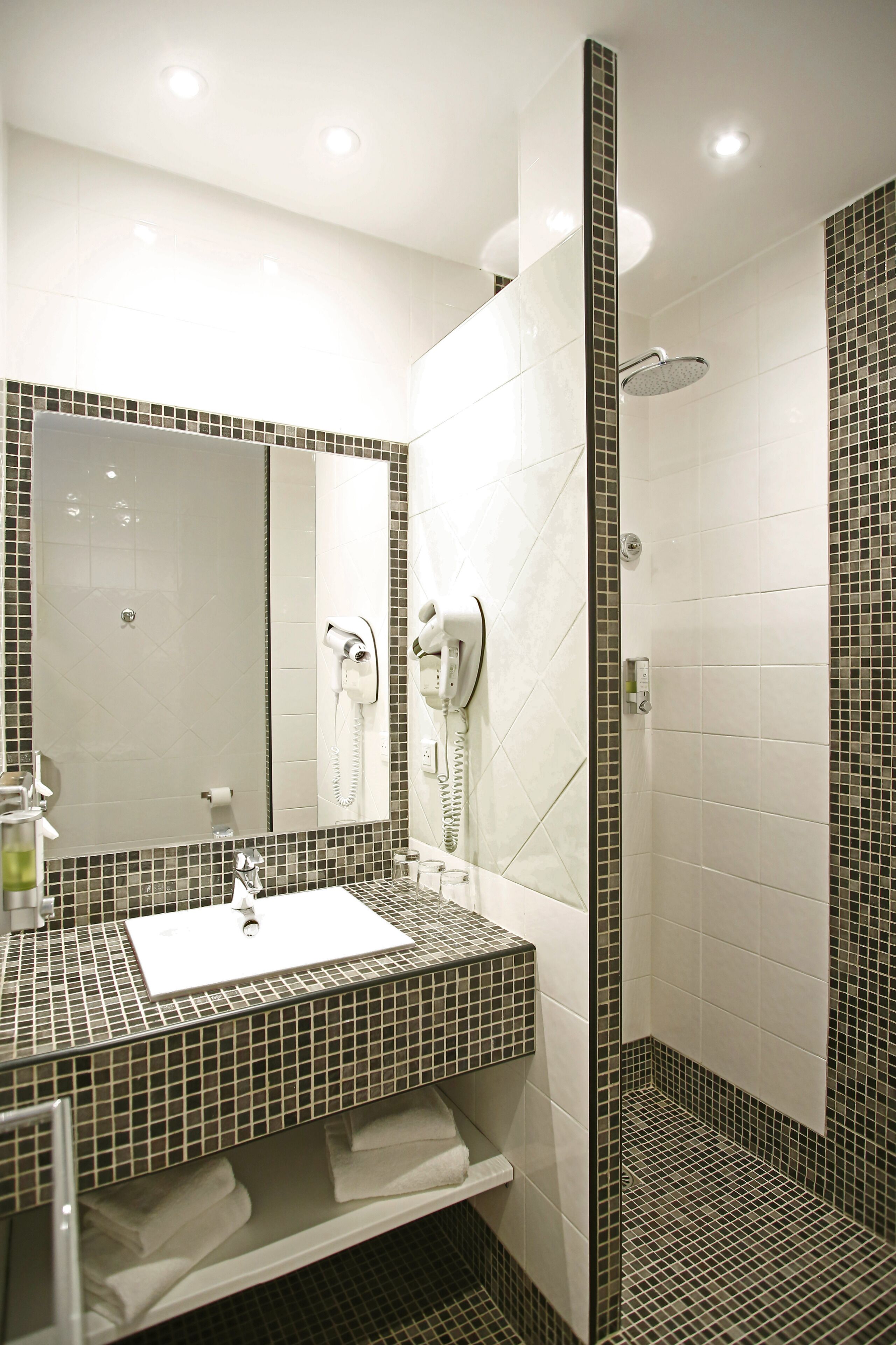 A bathroom with a tiled sink, a mirror, a hairdryer, and a shower.