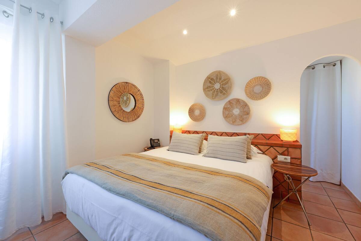 Uma cama bem arrumada com um cobertor listrado, uma mesinha de cabeceira com abajur e arte decorativa na parede.