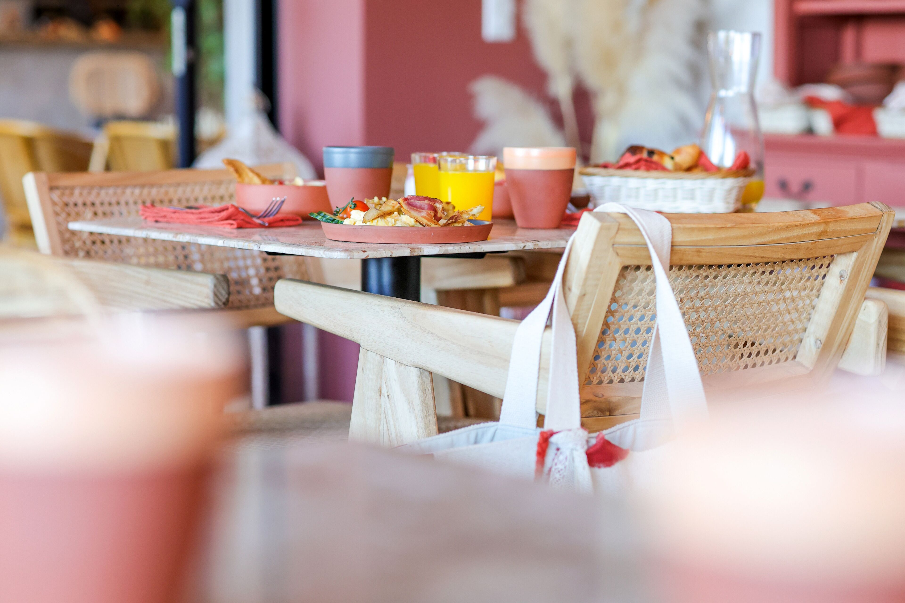 A dining area with wicker chairs and tables, a basket of food, and a pitcher of orange juice.