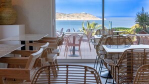Un espace extérieur aménagé pour les repas, avec des tables et des chaises en osier, une vue sur la mer et un phare visible au loin.