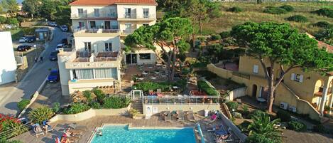 A hotel with a swimming pool, outdoor seating, and a view of the surrounding landscape.