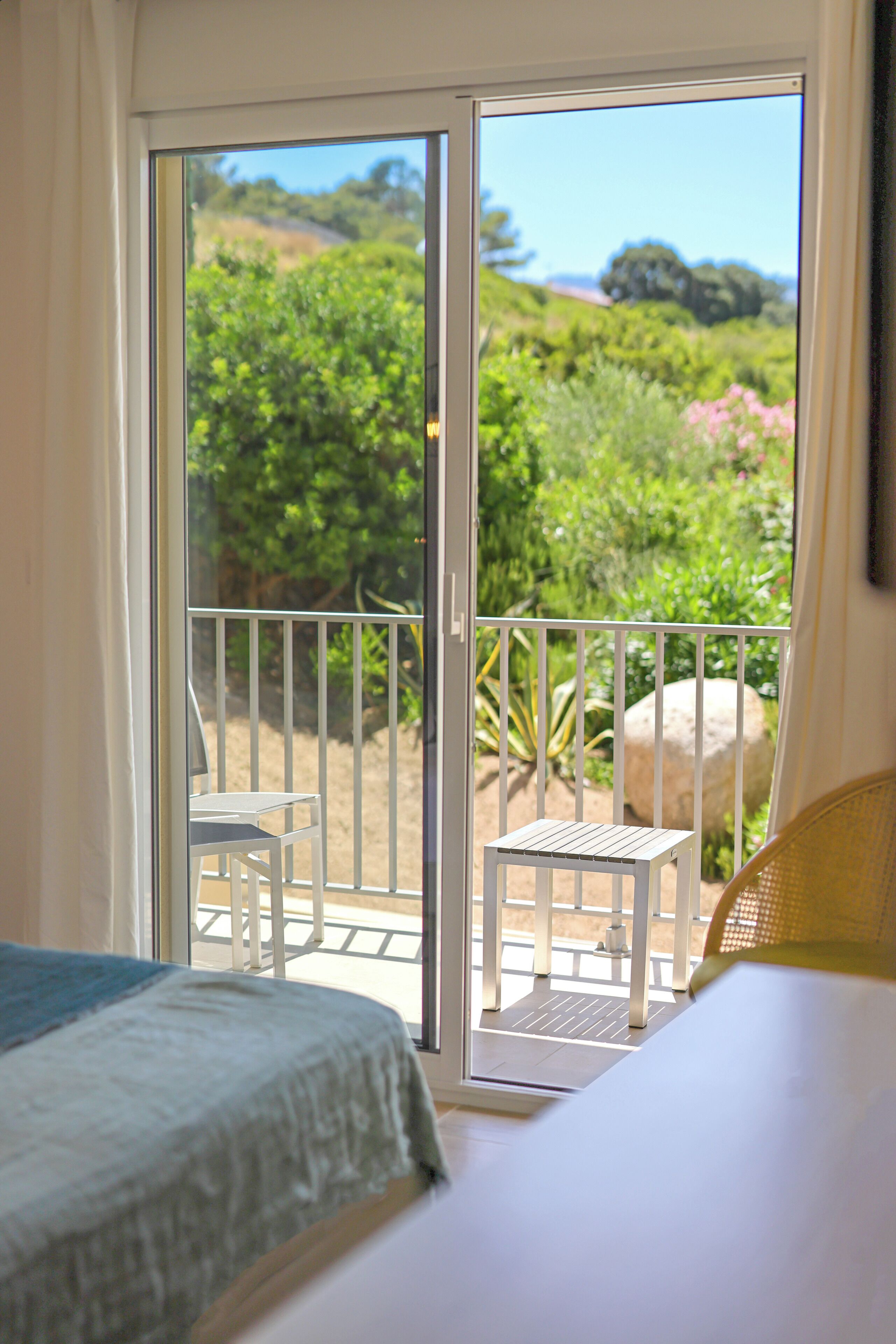 A bedroom with a balcony, a bed, a chair, and a small table.