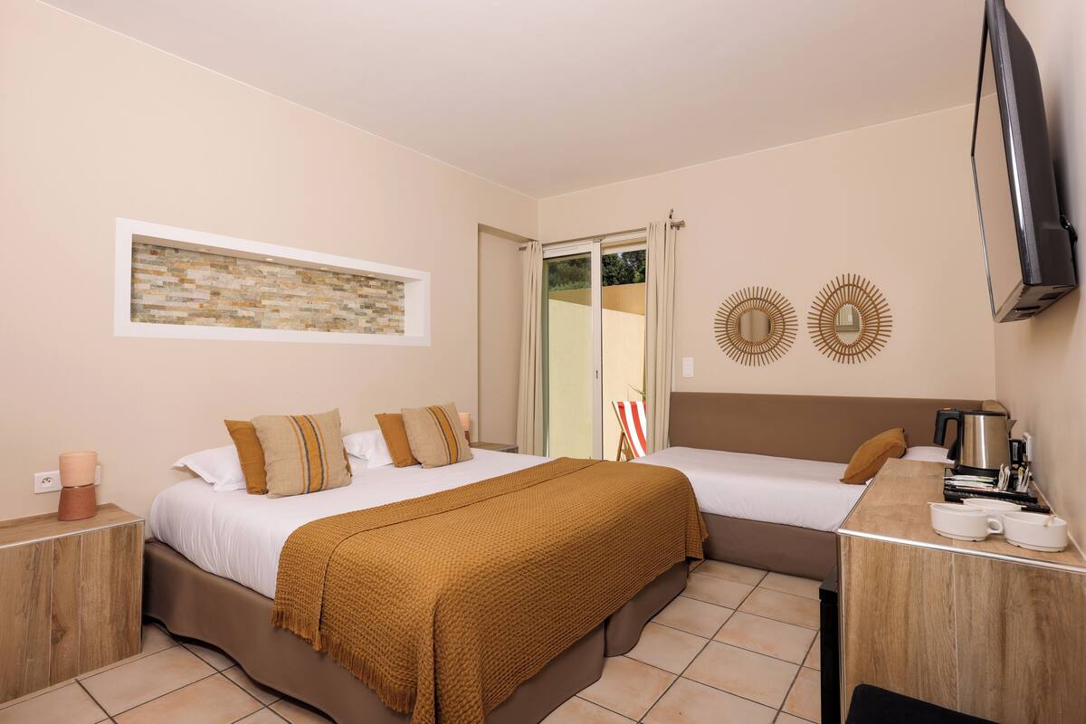 Quarto de hotel com duas camas, uma escrivaninha, televisão e janela com cortinas.