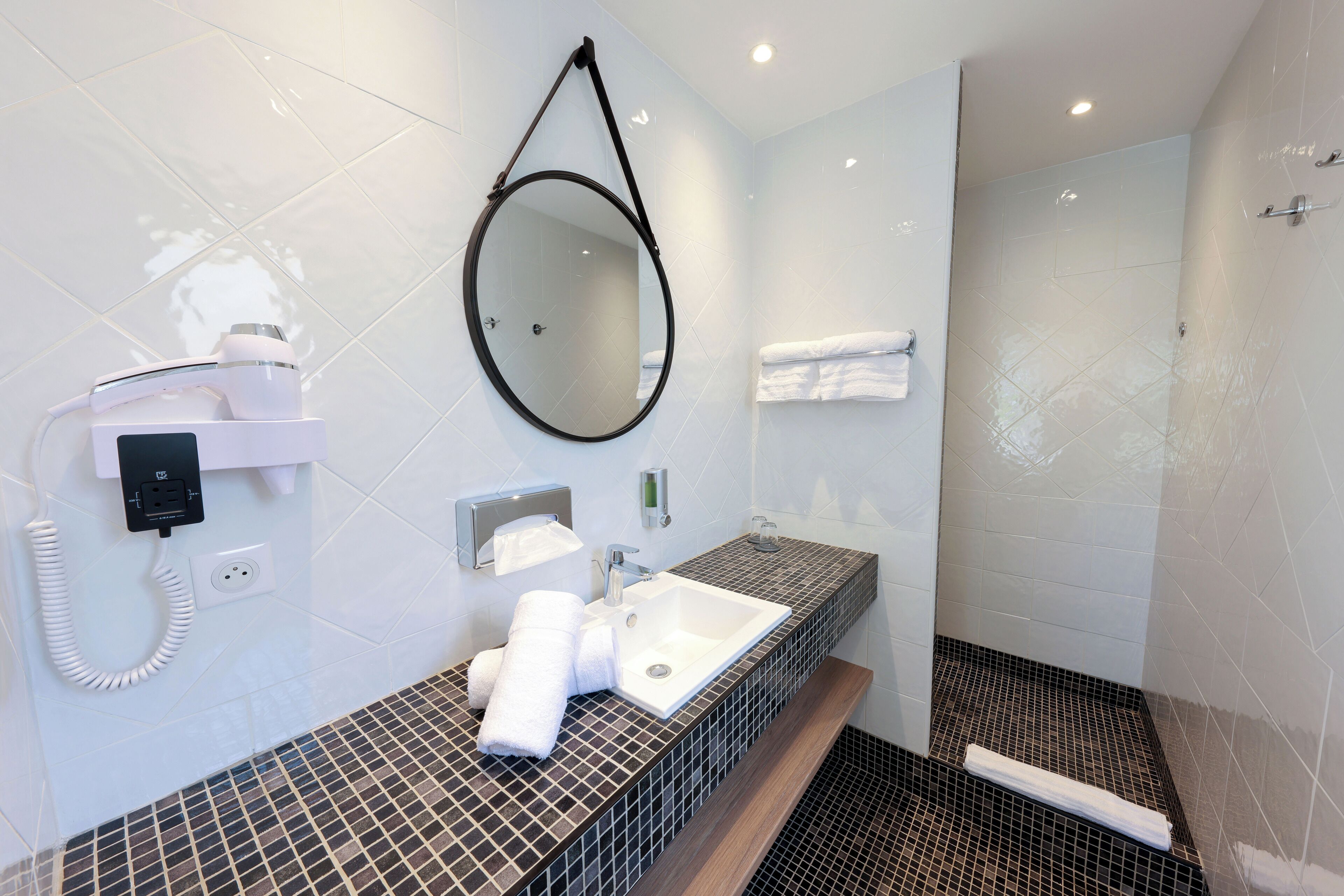Un baño moderno con suelo de baldosas, un lavabo con espejo arriba, un perchero y una zona de ducha.
