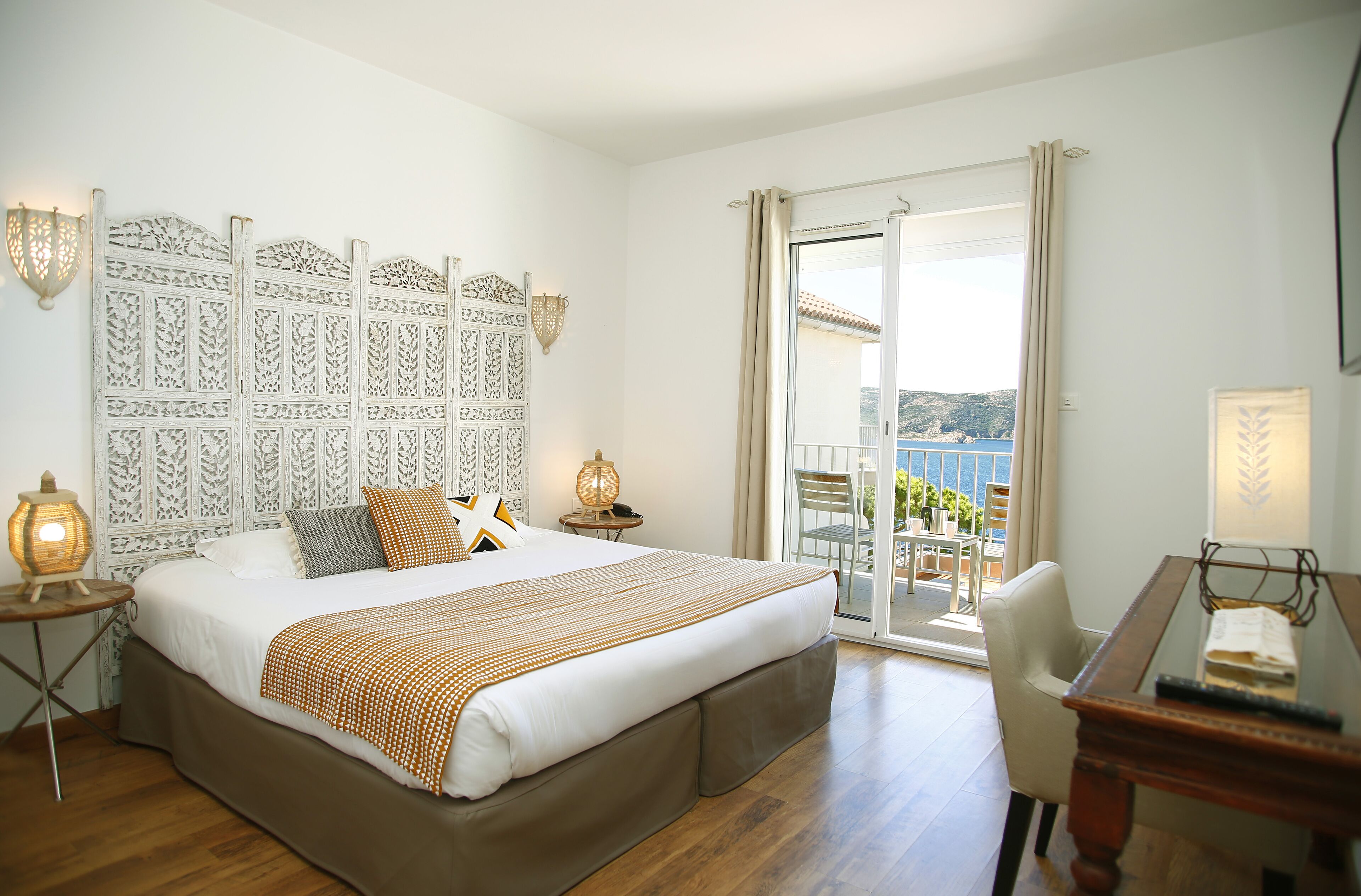 A hotel room with a large bed, a desk, a balcony with a view, and decorative wall panels.