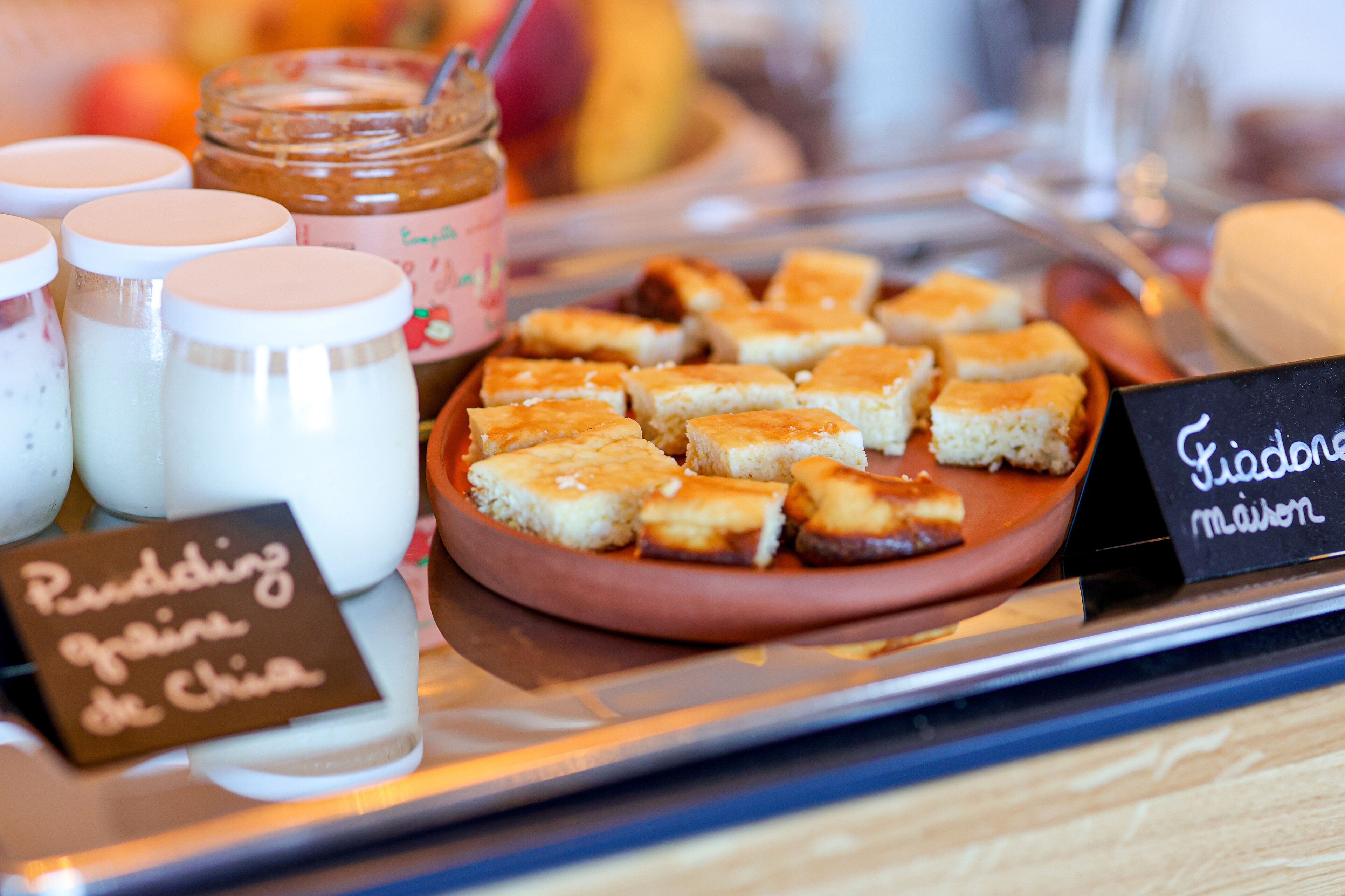 A tray of food items including bread, jars of condiments, and a sign indicating a pudding flavor.