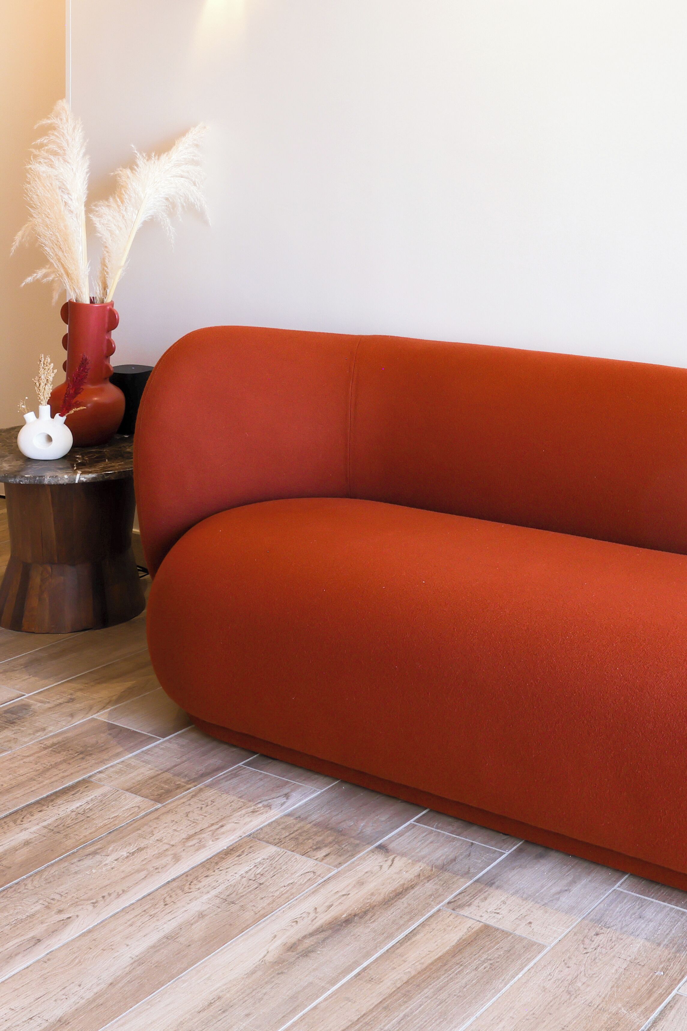 A modern living room with a sofa, a small side table, and a vase with pampas grass.