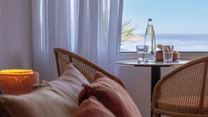 Une chambre d’hôtel avec un lit, une table sur laquelle se trouvent une bouteille et des verres, et une vue sur l’océan.