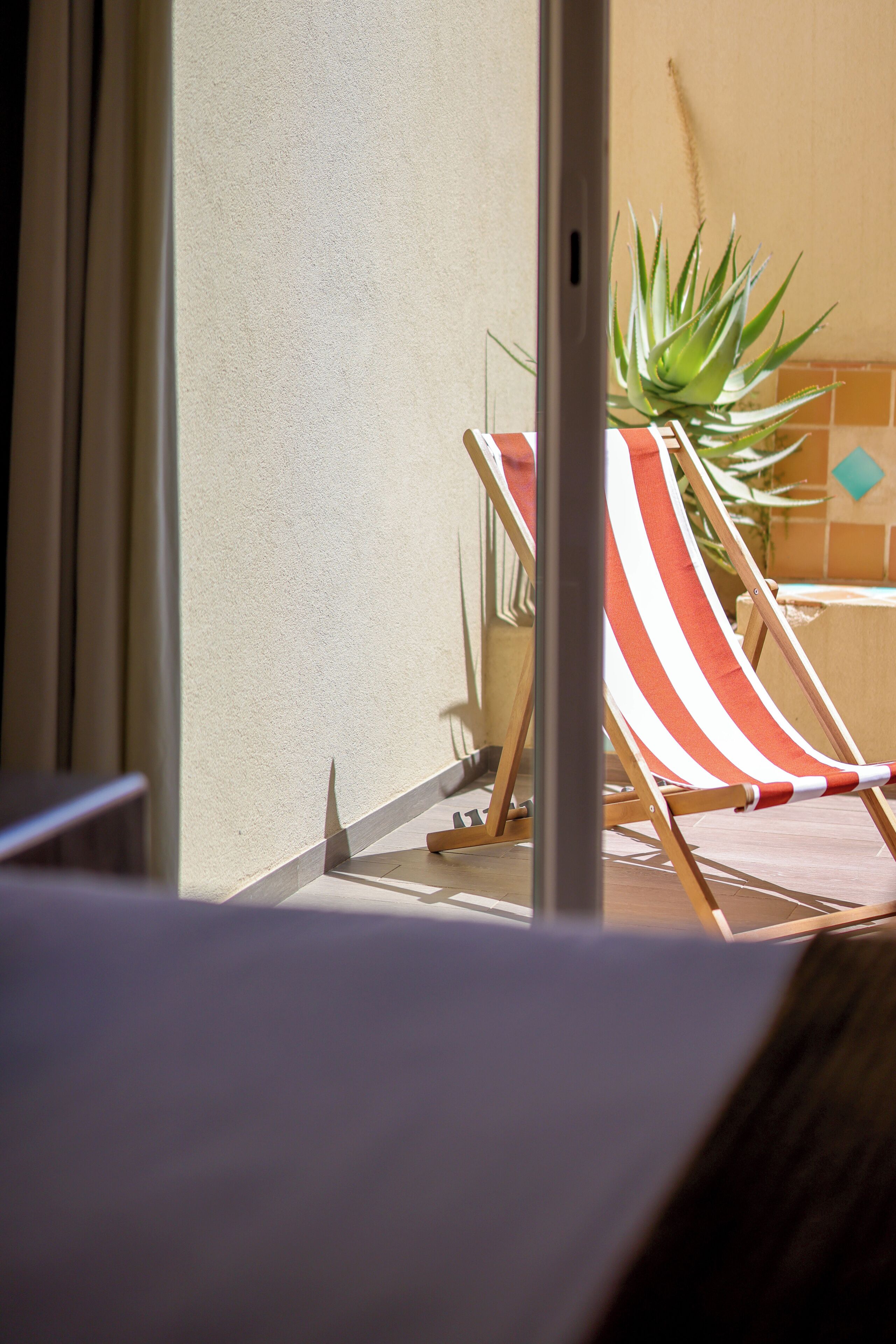 A beach chair with a striped cushion, a potted plant, and a tiled wall.