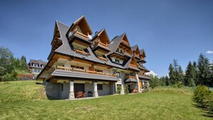 A large, multi-story chalet with a steeply pitched roof, wooden balconies, and a stone foundation. - VisitZakopane Vanilla Apartments (Koscielisko)