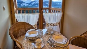 A dining table set with plates, glasses, and cutlery, positioned near a window with a view of snow-capped mountains. - VisitZakopane Vanilla Apartments (Koscielisko)