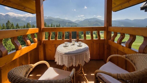 A wooden deck with wicker chairs and a table, overlooking a mountainous landscape. - VisitZakopane Vanilla Apartments (Koscielisko)