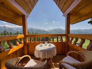A wooden deck with wicker chairs and a table, overlooking a mountainous landscape. - VisitZakopane Vanilla Apartments (Koscielisko)