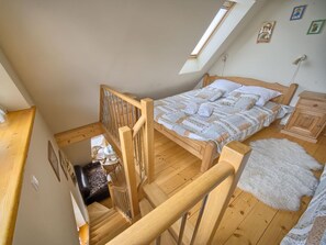 A bedroom with a wooden bed, a small bedside table, a white furry rug, and a skylight. - VisitZakopane Vanilla Apartments (Koscielisko)