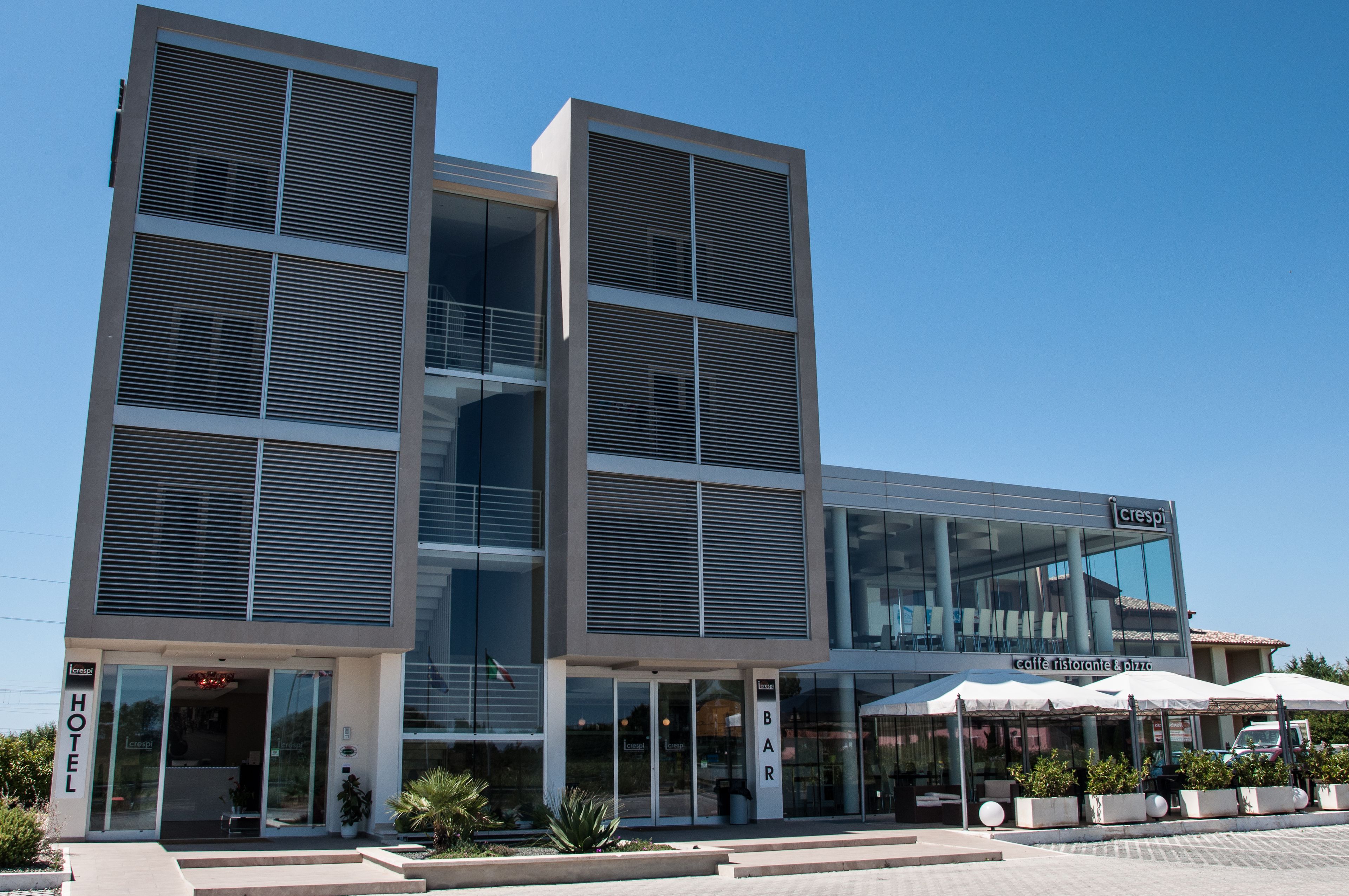 Een modern hotel met een glazen gevel, een barruimte met terras en een zichtbare ingang.