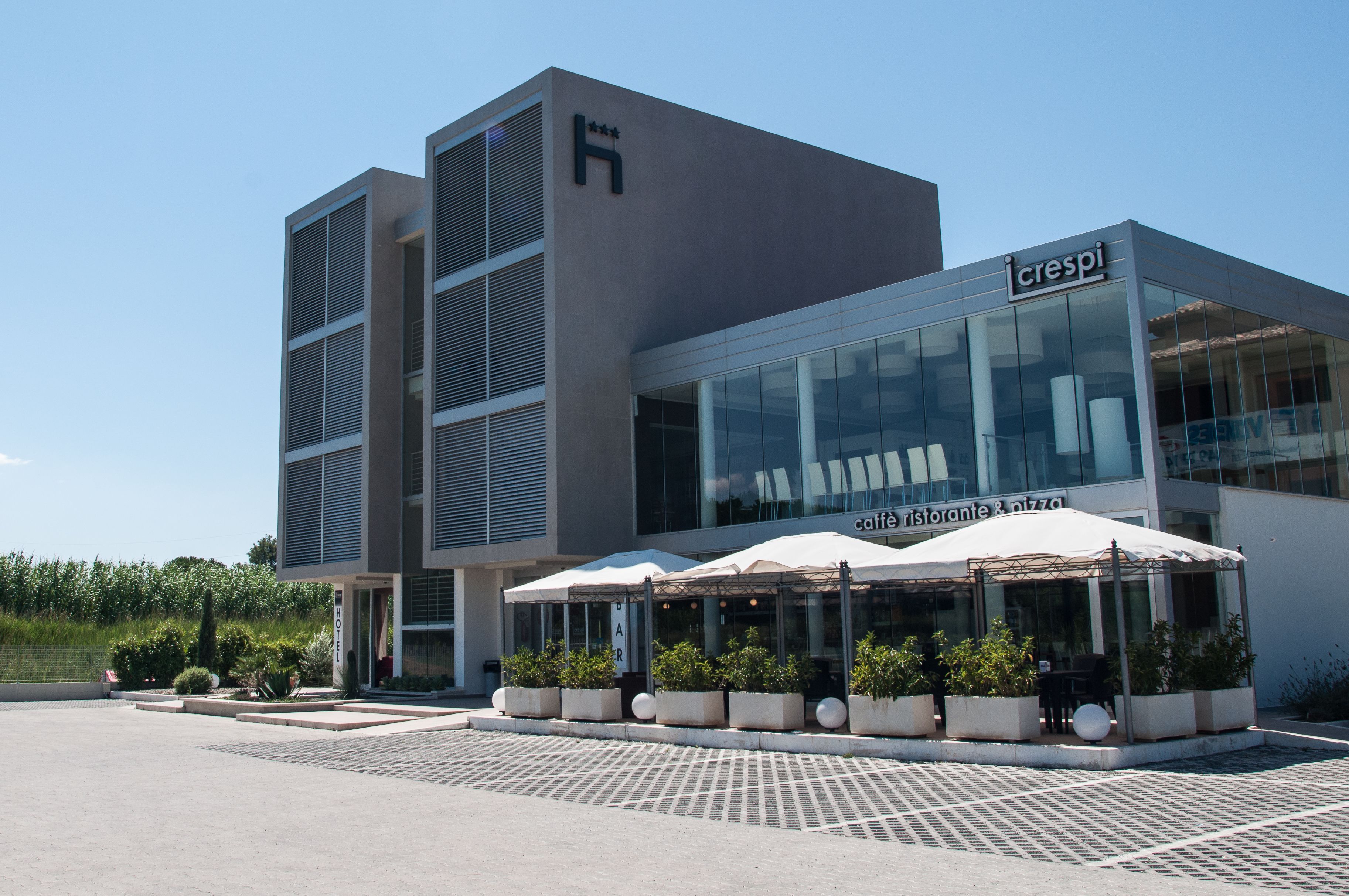 Un edificio moderno con cafetería y restaurante en la planta baja, con terraza al aire libre y sombrillas.