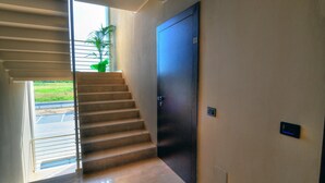 Un interior moderno con una escalera que conduce a una puerta, una planta pequeña y un panel de control fijado a la pared.
