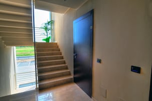 A modern interior with a staircase leading to a door, a small plant, and a wall-mounted control panel.