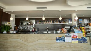 Una zona de bar con encimera de mármol, luces colgantes, estanterías con botellas y carteles promocionales.