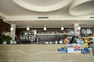 A bar area with a marble countertop, hanging lights, shelves with bottles, and promotional posters.